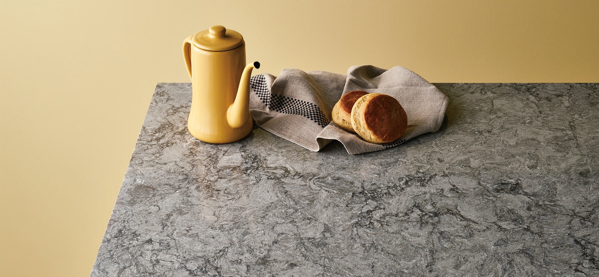 yellow teapot on turbine grey counters with bread and brown towel
